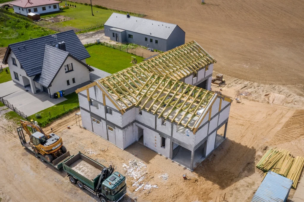 Dom w trakcie budowy z widoczną konstrukcją dachu na ujęciu z drona